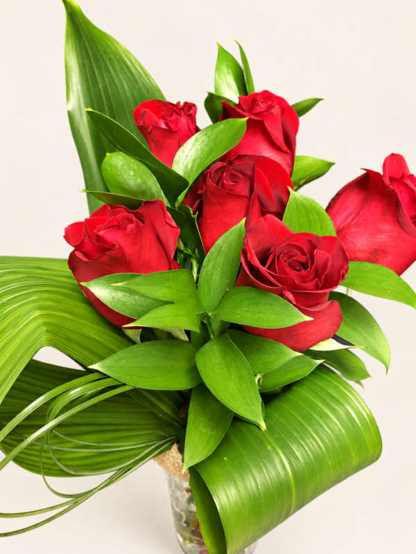 Bouquet de six roses rouges avec feuillage dans un vase sur fond neutre