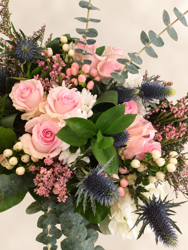 Bouquet de roses roses, fleurs blanches et chardons bleus sur fond neutre