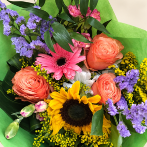 Bouquet coloré avec roses pêche, gerbera rose, tournesol et papier vert sur fond neutre