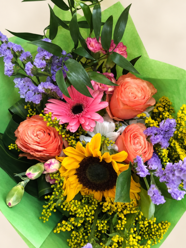 Bouquet coloré avec roses pêche, gerbera rose, tournesol et papier vert sur fond neutre