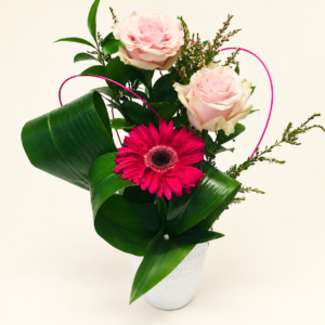 Un gerbera fuchsia et deux roses rose pâle dans un vase blanc sur fond ivoire