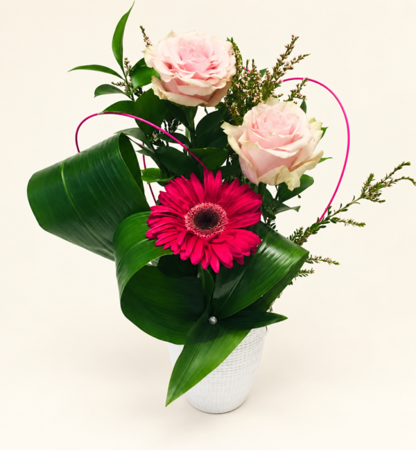 Un gerbera fuchsia et deux roses rose pâle dans un vase blanc sur fond ivoire