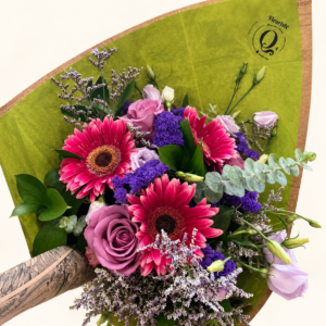 Bouquet Julie, gerberas roses et fleurs mauves avec papier de soie vert et emballage Q4 sur fond ivoire