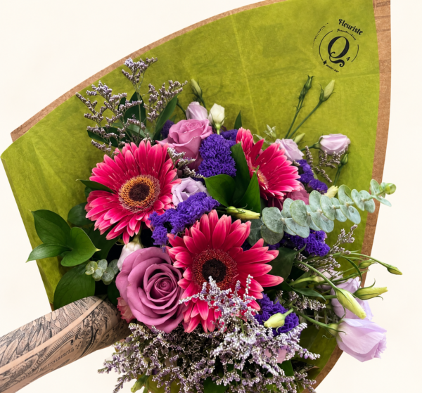 Bouquet Julie, gerberas roses et fleurs mauves avec papier de soie vert et emballage Q4 sur fond ivoire