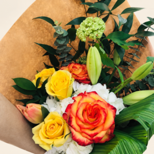 Bouquet coloré avec rose orange bordée de rouge et roses jaunes dans son emballage sur fond crème