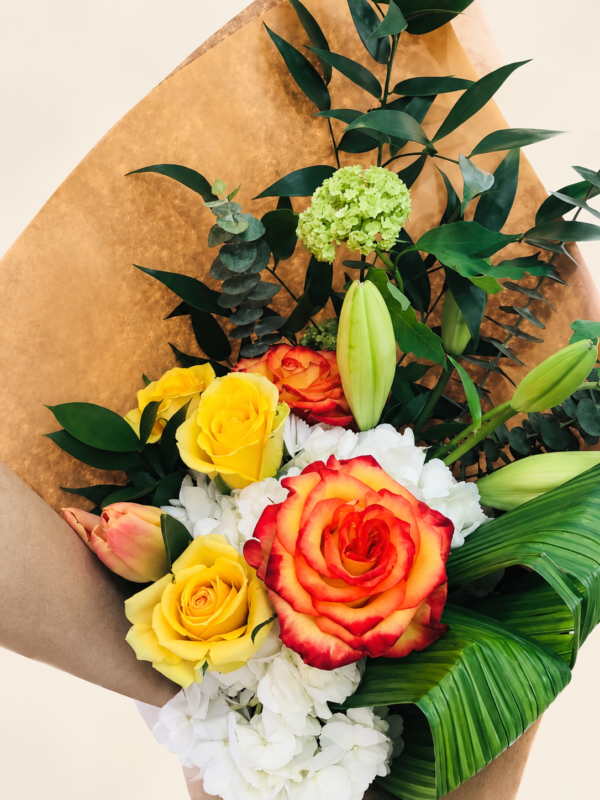 Bouquet coloré avec rose orange bordée de rouge et roses jaunes dans son emballage sur fond crème