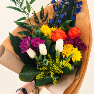 Bouquet de fleurs coloré Alex tenu à la main, sur fond crème pâle