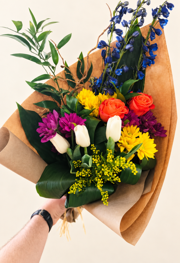 Bouquet de fleurs coloré Alex tenu à la main, sur fond crème pâle