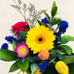 Bouquet multicolore avec gerbera jaune, rose rouge et fleurs bleues sur fond crème pâle