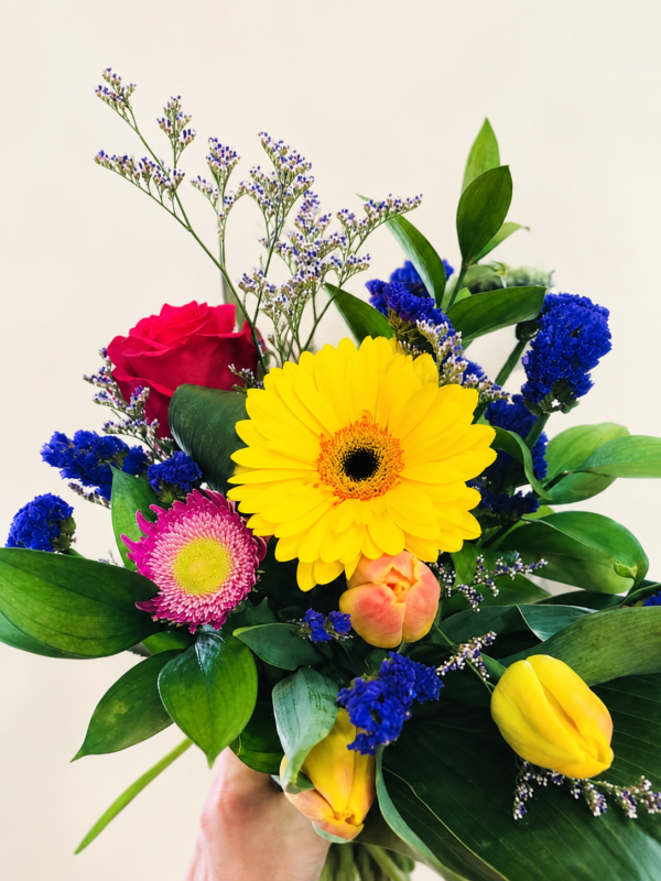 Bouquet multicolore avec gerbera jaune, rose rouge et fleurs bleues sur fond crème pâle